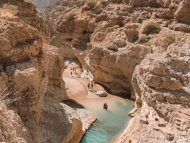 Tourists walking and wading through the rocky canyon of Wadi Shab.