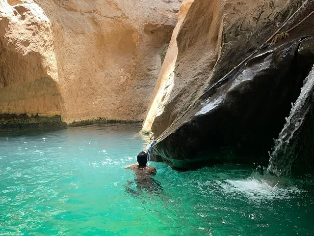 Een persoon die zwemt bij een kleine waterval in een rotsachtige grot of canyon.
