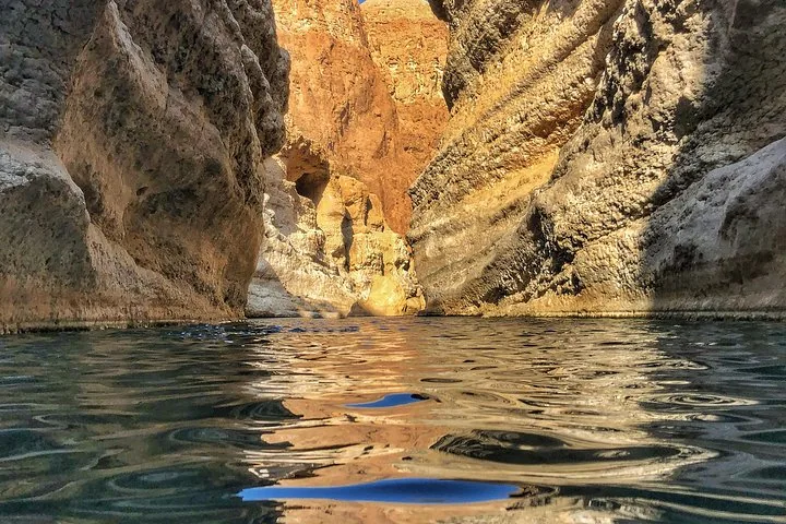 Uitzicht op waterniveau door een smalle, door de zon verlichte rotskloof in Wadi Shab.