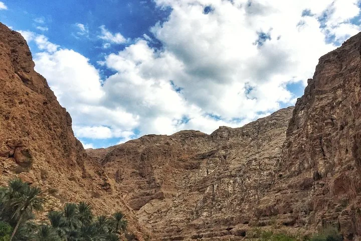Hoge, ruige rotswanden van de kloof van Wadi Shab onder een halfbewolkte lucht.