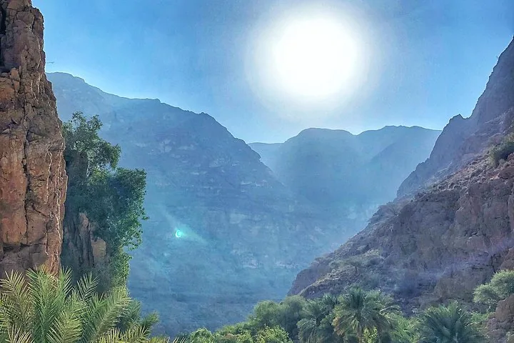 Die Sonne scheint hell über den tiefen Schluchtwänden und dem Grün des Wadi Shab.