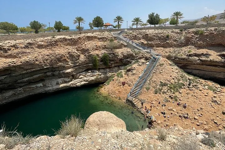 Touristen entspannen und schwimmen am Bimmah Sinkhole, das über eine lange Treppe erreichbar ist.