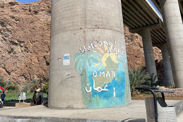 Ein bemaltes Willkommensschild für Wadi Shab an einem Betonpfeiler unter einer Brücke.