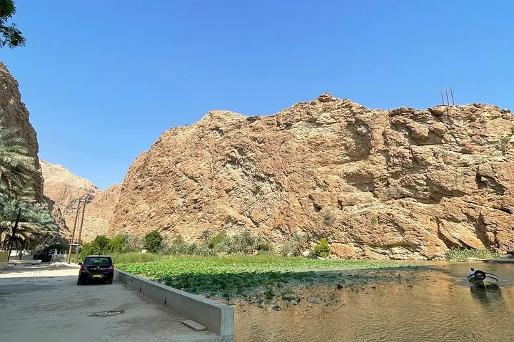 De ingang van Wadi Shab met een boot op het water en torenhoge kliffen.