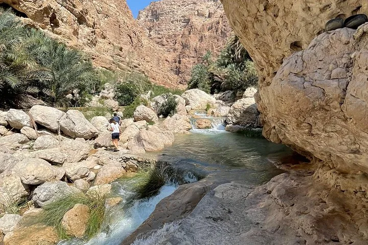 Un ruscello scorre sulle rocce mentre alcune persone camminano nel canyon di Wadi Shab.