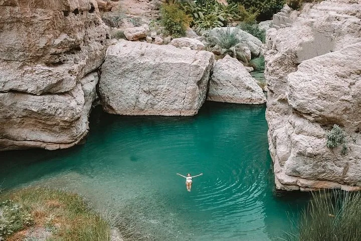Een vrouw drijft rustig in het heldere turquoise water van Wadi Shab.