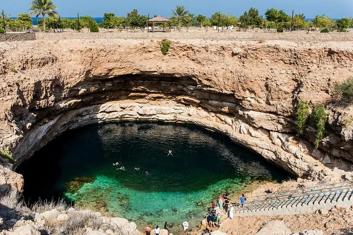 Vista dall'alto su Bimmah Sinkhole, dove alcune persone nuotano nell'acqua azzurra e cristallina.